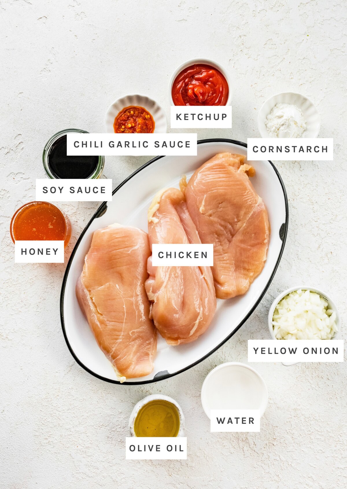 All ingredients measured out to make Slow Cooker Teriyaki Chicken: Chicken, ketchup, cornstarch, chili garlic sauce, soy sauce, honey, yellow onion, water, olive oil.
