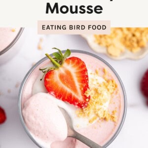 Glass of high-protein strawberry mousse topped with yogurt, crushed cookies, and a fresh strawberry half, with a spoonful scooped out.