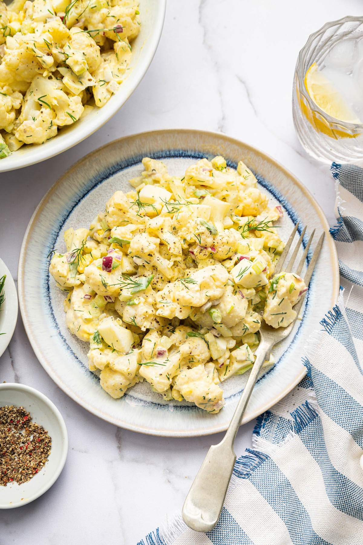 Cauliflower potato salad served on a plate with a silver fork. The salad is topped with fresh dill.