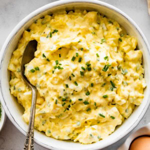 Cottage cheese egg salad served in a white ceramic bowl served with a silver spoon. Fresh chives are topping the egg salad.