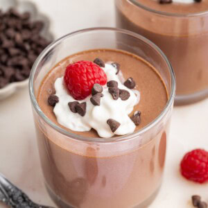 Cottage cheese chocolate mousse in two glasses topped with whip cream, chocolate chips and fresh raspberries.