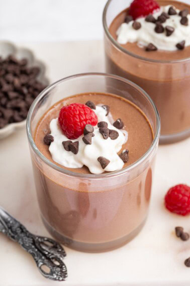Cottage cheese chocolate mousse in two glasses topped with whip cream, chocolate chips and fresh raspberries.