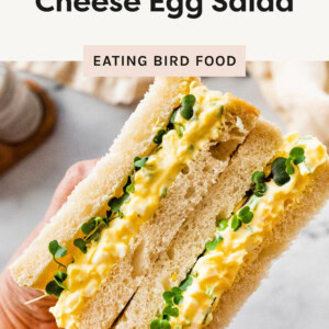 A hand holding a sandwich made with soft white bread, filled with creamy cottage cheese egg salad.