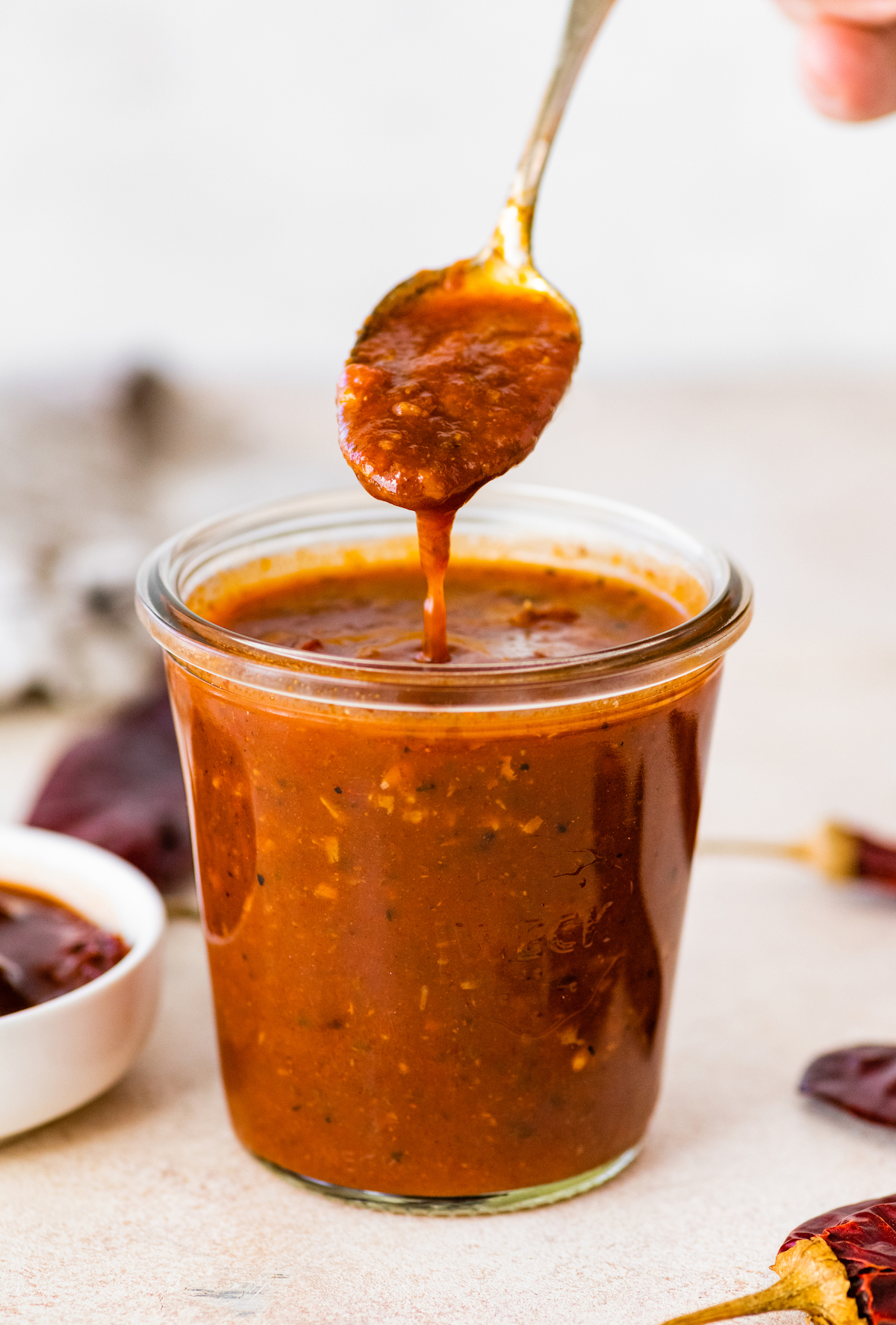 Homemade enchilada sauce in a glass weck jar. A gold spoon is scooping some of the sauce out from the glass.