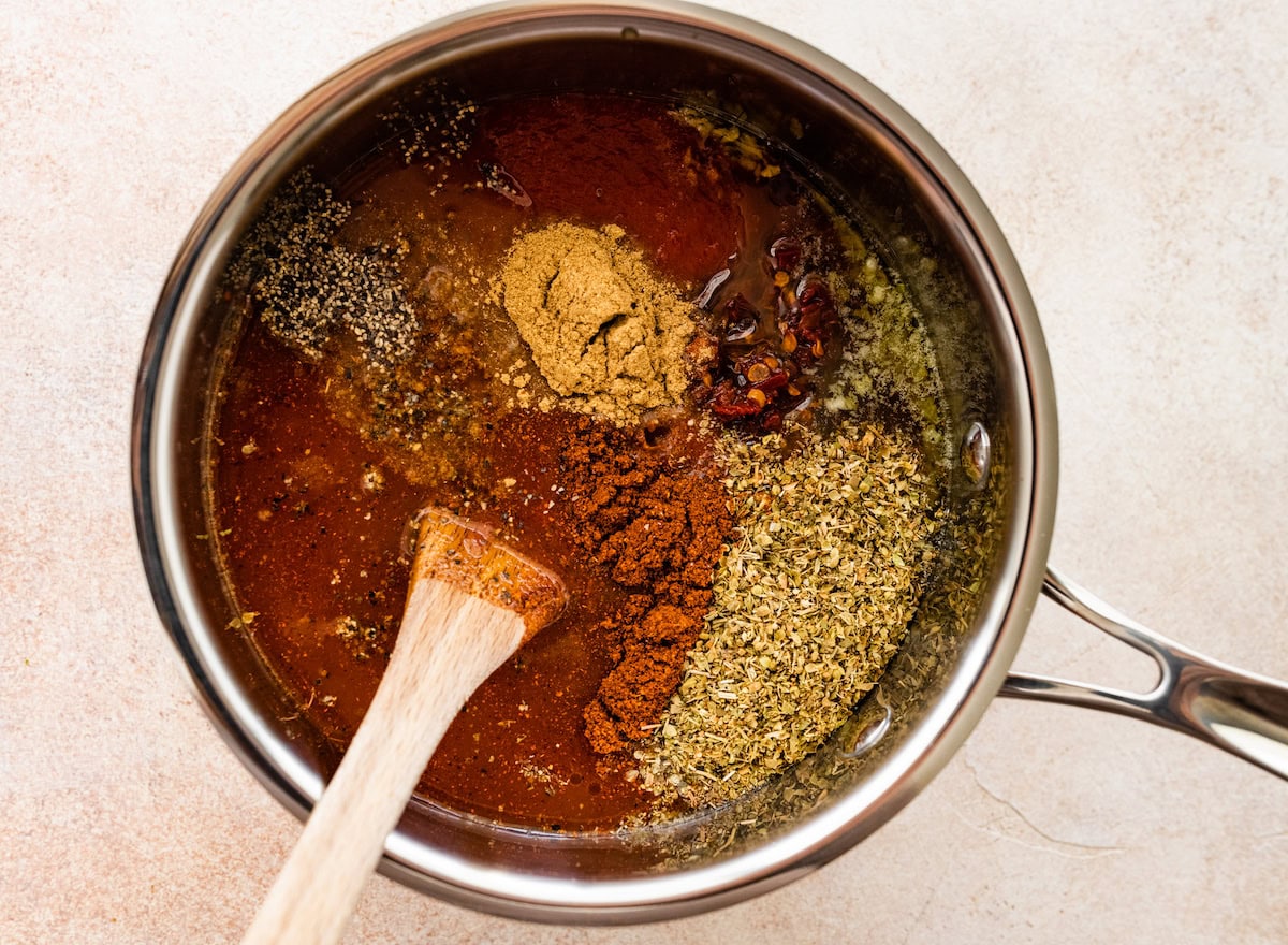 Homemade enchilada sauce being mixed together in a pot with a wooden spoon.