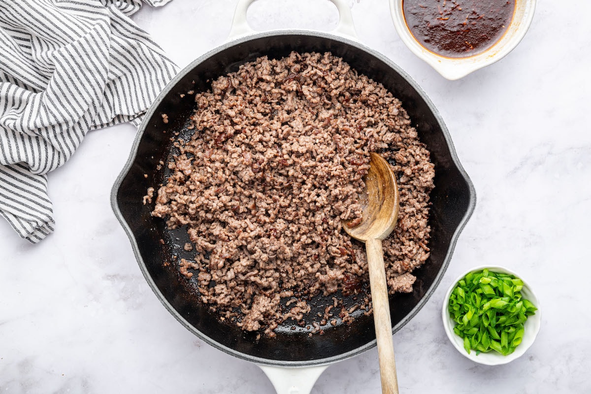Cooked ground beef in a skillet. There is a wooden spoon in the skillet.