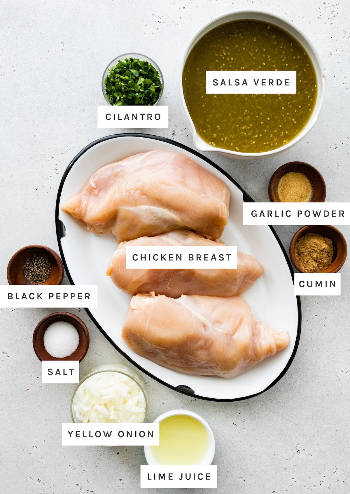 Ingredients measured out to make Salsa Verde Chicken: Chicken breast, salsa verde, garlic powder, cumin, black pepper, salt, yellow onion, lime juice, cilantro.