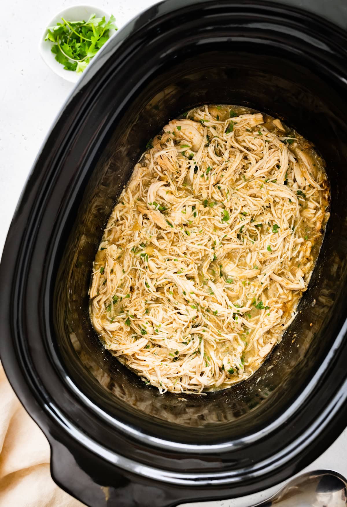Shredded salsa verde chicken in a slow cooker with chopped fresh cilantro on top.
