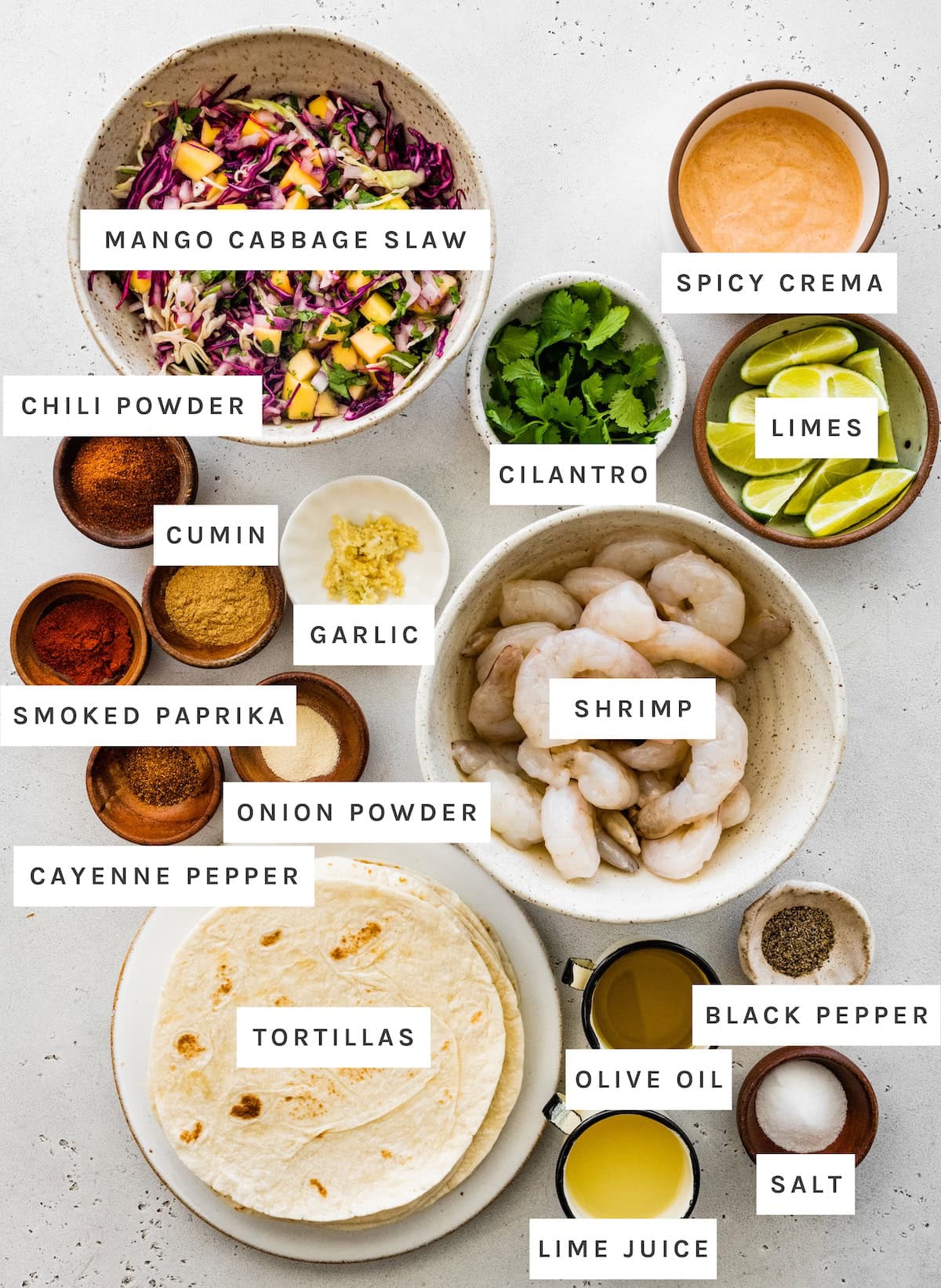 Shrimp Tacos with Mango Cabbage Slaw ingredients: cabbage slaw, spicy crema, chili powder, cumin, garlic, smoked paprika, onion powder, cayenne pepper, tortillas, shrimp, cilantro, limes, olive oil, lime juice, black pepper, salt.