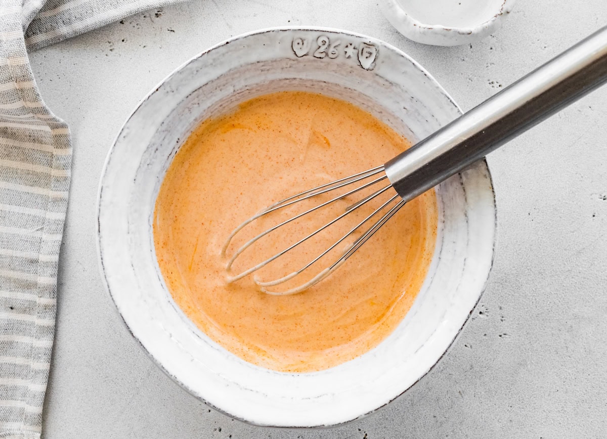 The spicy crema whisked together in a small bowl. There is a whisk in the bowl.