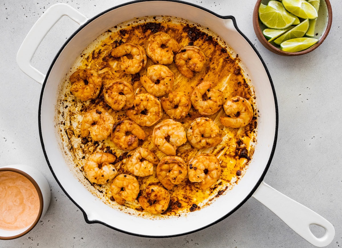 Cooked shrimp for the shrimp tacos in a skillet next to a small bowl with limes.