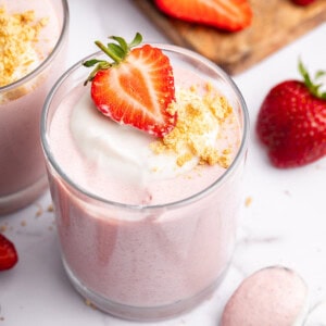 One glass filled with high-protein strawberry mousse topped with a dollop of cocowhip, one halved fresh strawberry and crushed graham crackers.