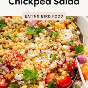Colorful quinoa chickpea salad in a white bowl, mixed with fresh veggies, feta, and parsley,