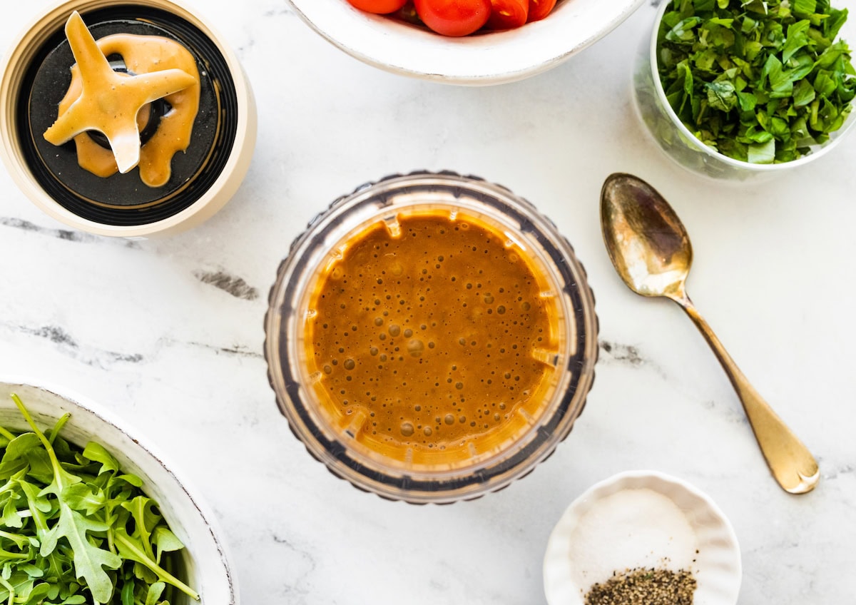 The balsamic dressing in a blender next to a gold spoon.