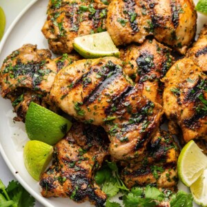 Grilled chicken thighs on a plate garnished with fresh cilantro and lime wedges.