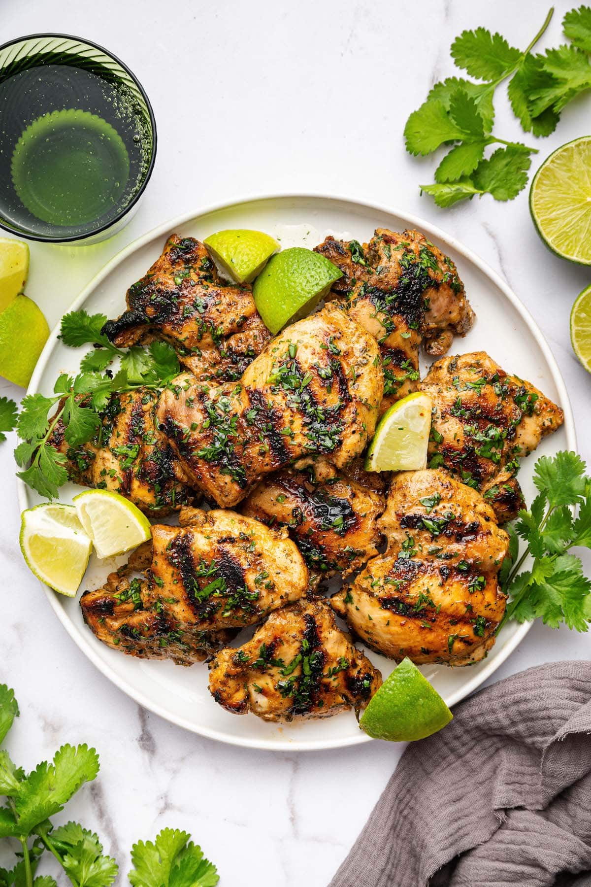 Cooked chicken thighs on a white plate garnished with fresh cilantro and lime wedges.