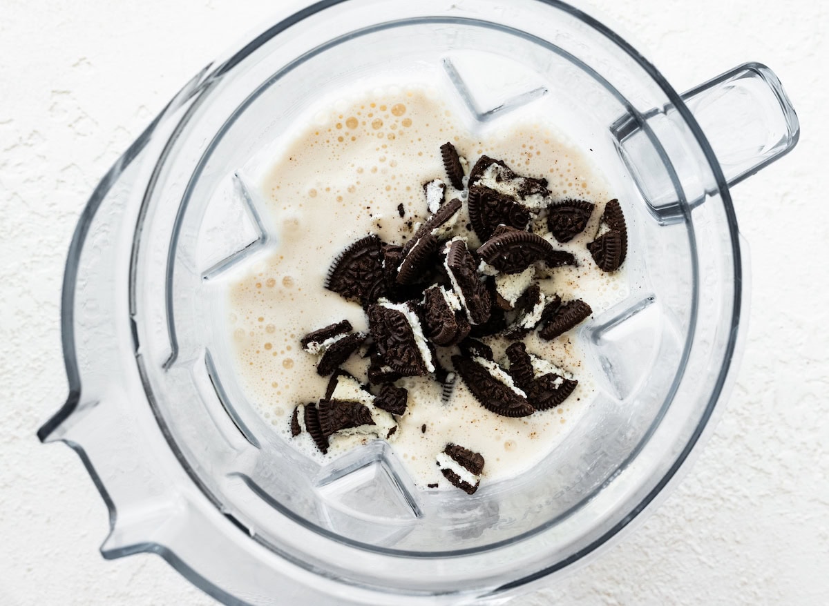 Crushed chocolate sandwich cookies added to a blender filled with a vanilla protein shake base, before blending into a cookies and cream shake.