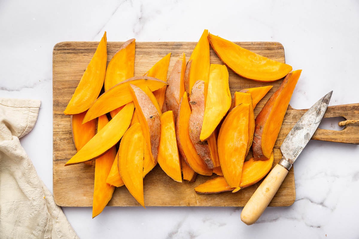 Sliced sweet potato wedges on a wooden cutting board next to a knife.