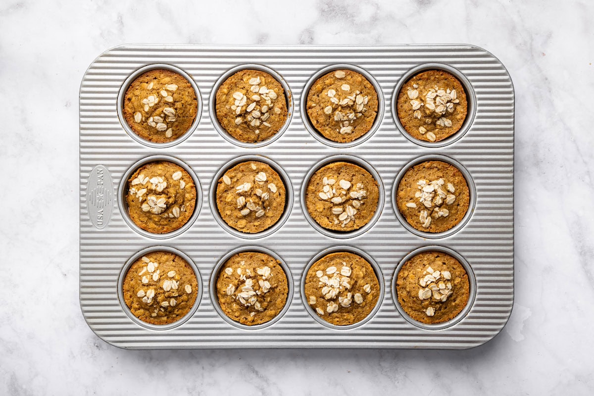 Baked applesauce muffins in a muffin tin, topped with oats and fresh from the oven.