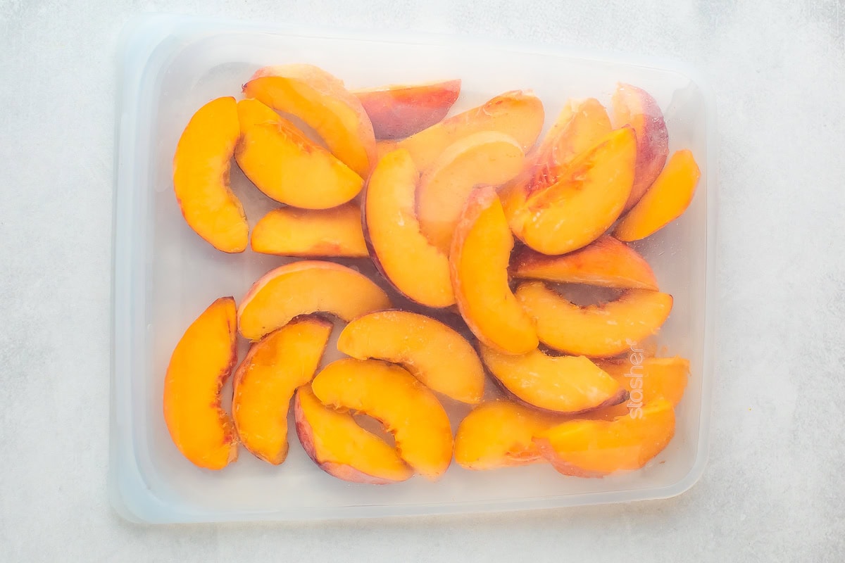 A plastic container filled with sliced peaches.