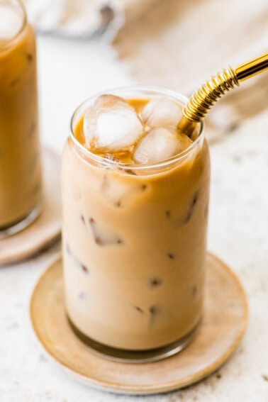 Finished iced coffee with a creamy light brown color and ice cubes, served with a gold metal straw.