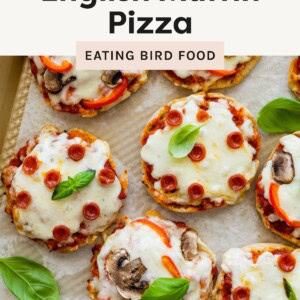 ChatGPT said: Overhead view of mini English muffin pizzas topped with melted cheese, mini pepperoni, red peppers, mushrooms, and basil leaves on a baking sheet.
