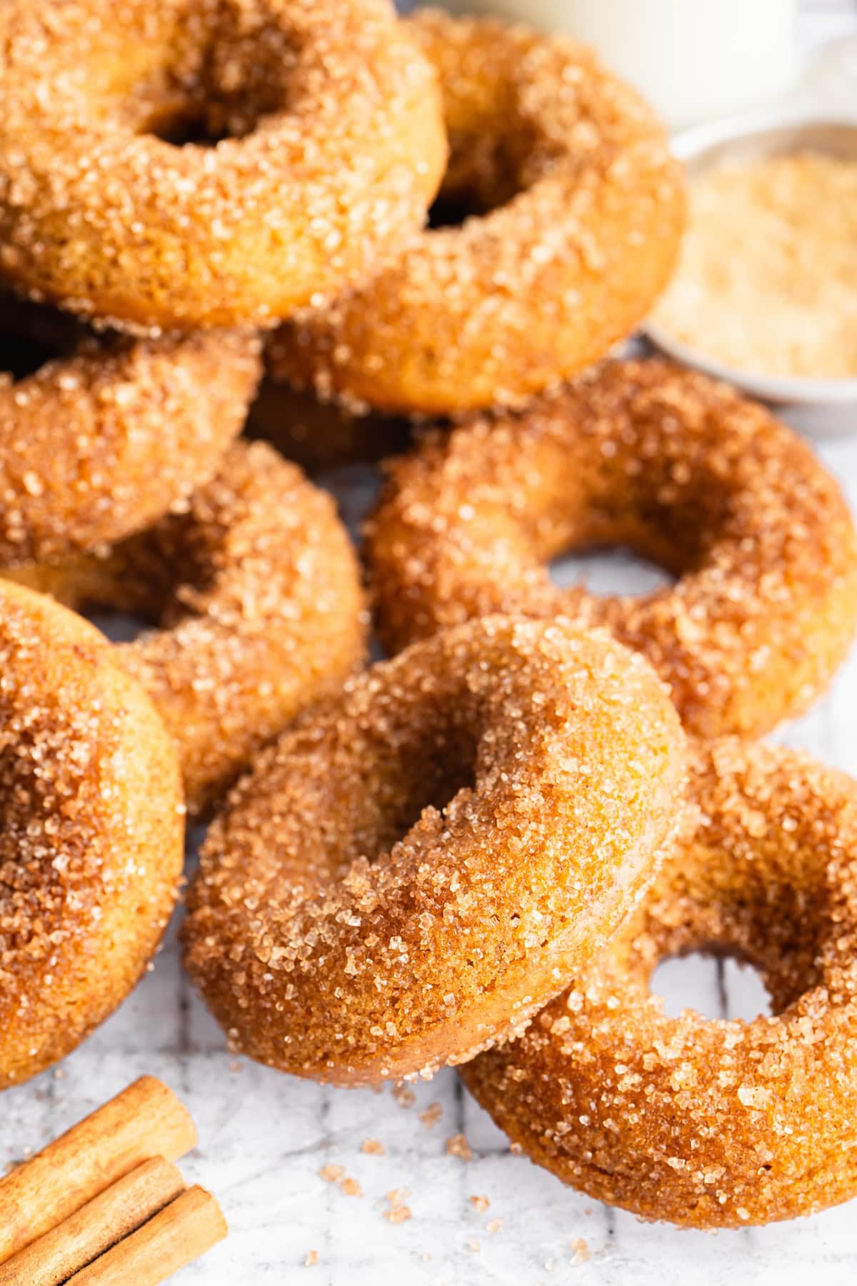 Pile of donuts coated in cinnamon sugar with cinnamon sticks and milk in the background.