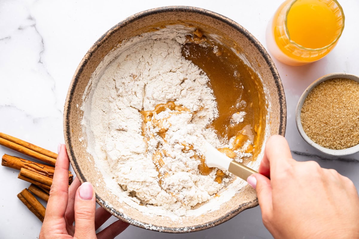 Donut batter being gently mixed with flour in a ceramic mixing bowl.