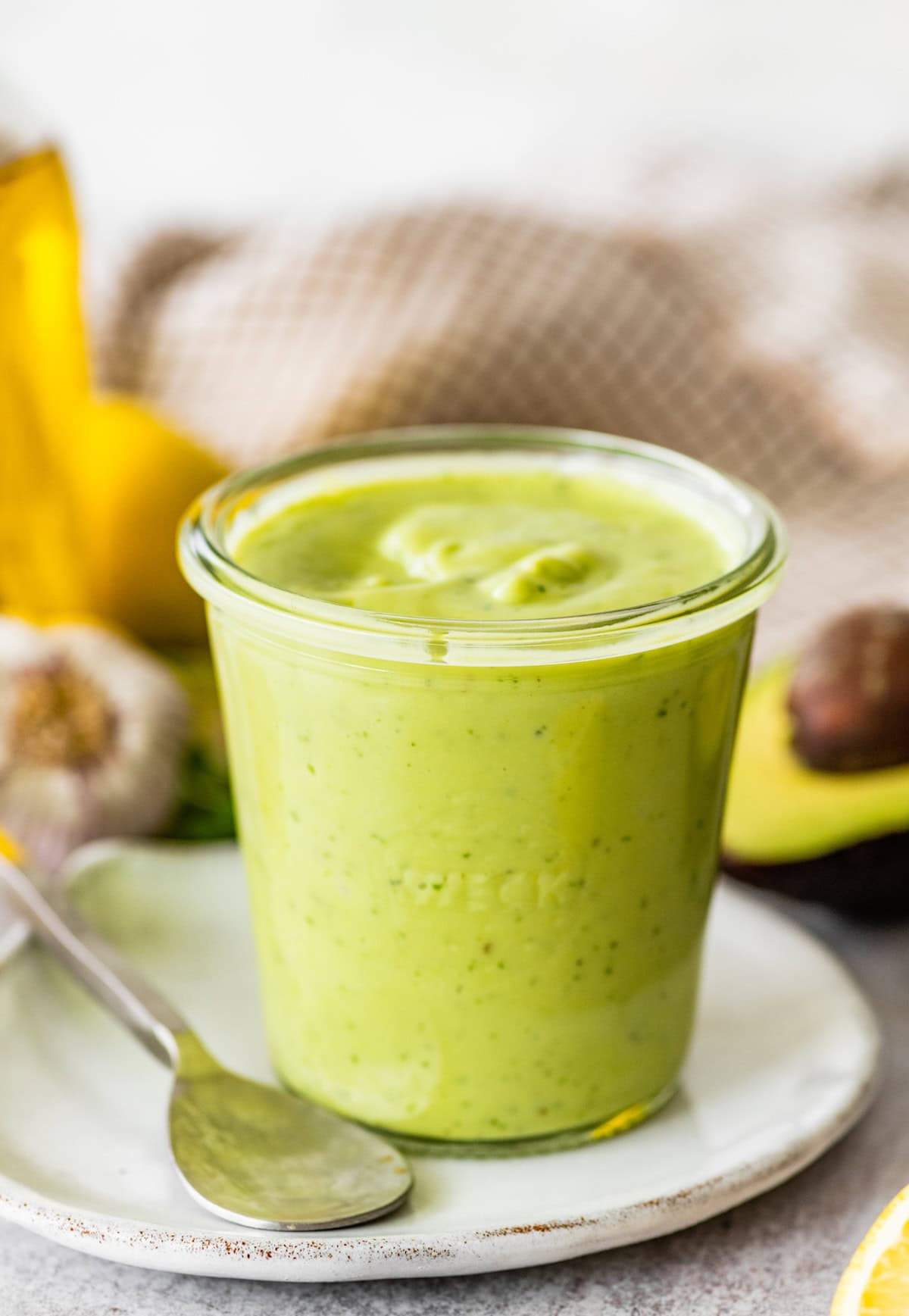 Creamy avocado dressing in a glass weck jar served on a plate alongside a spoon.