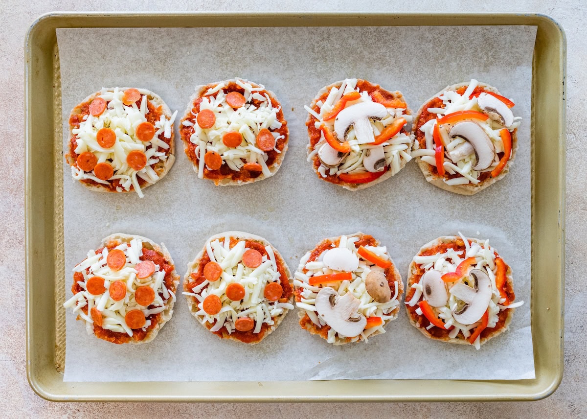 English muffins topped with sauce, cheese, and toppings before baking.