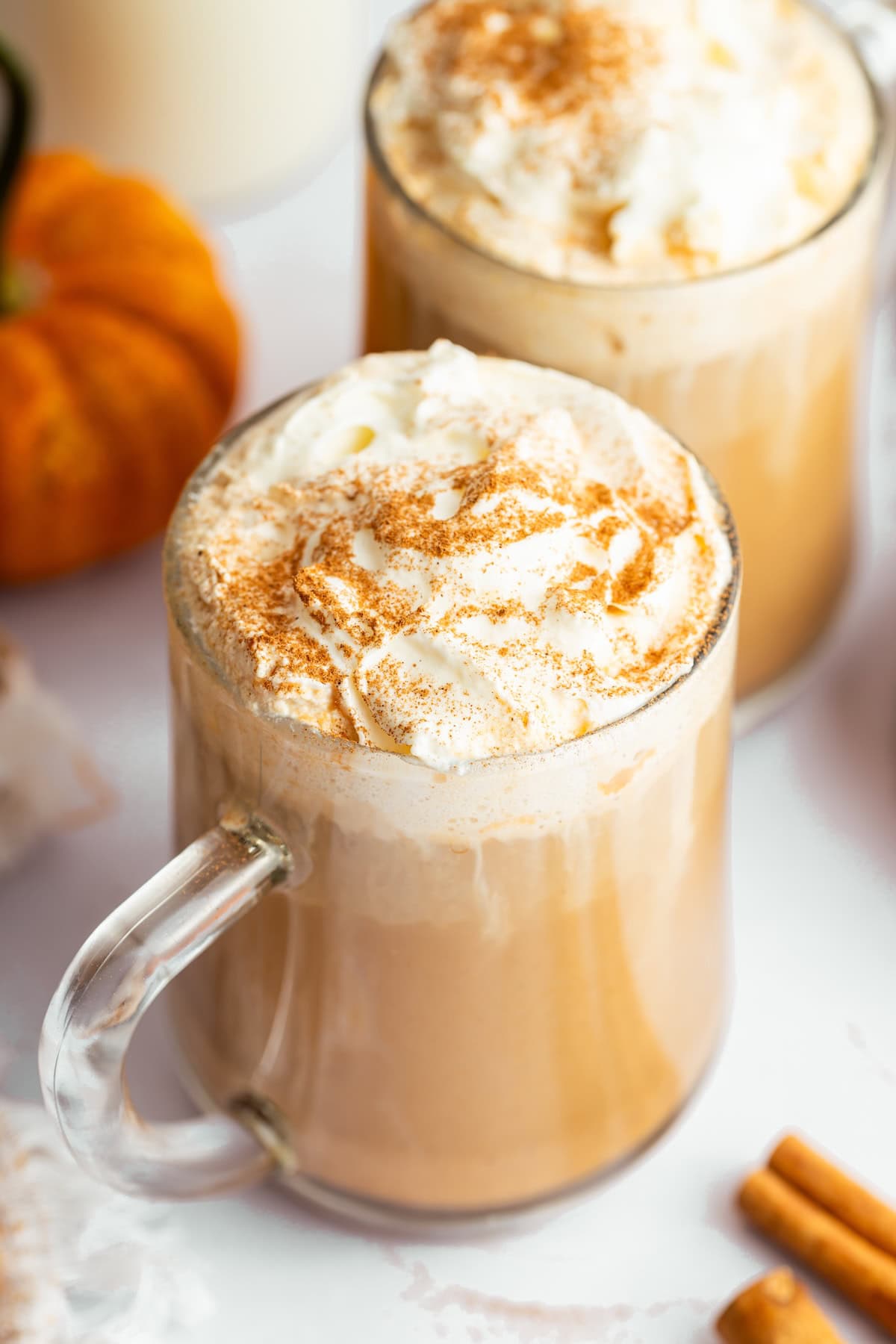 Homemade pumpkin spice latte in a glass mug topped with whipped cream and a sprinkle of cinnamon.