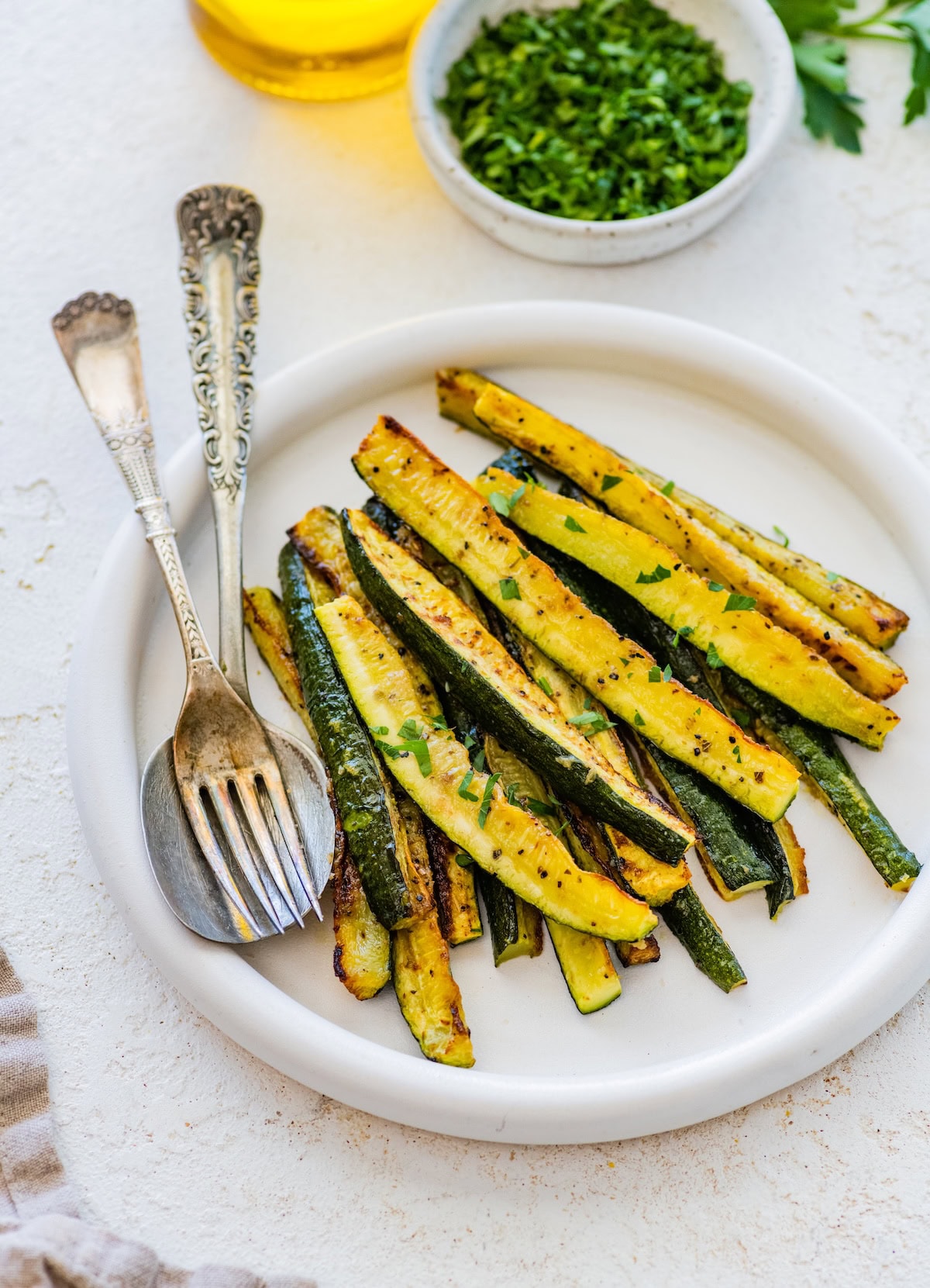 Roasted zucchini sticks topped with fresh herbs, served on a white plate.
