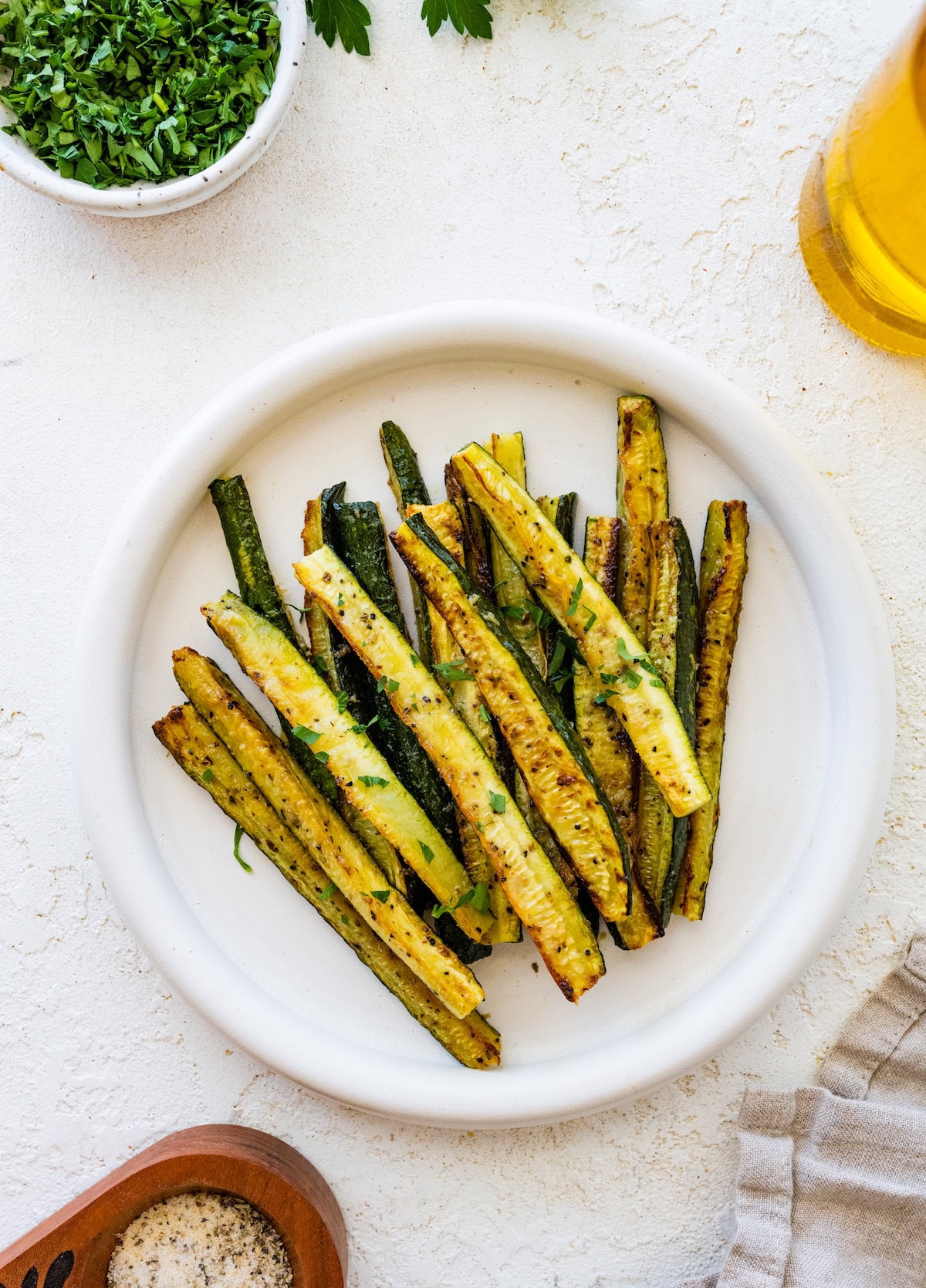 Oven roasted zucchini sticks on a white plate, golden brown and ready to serve.