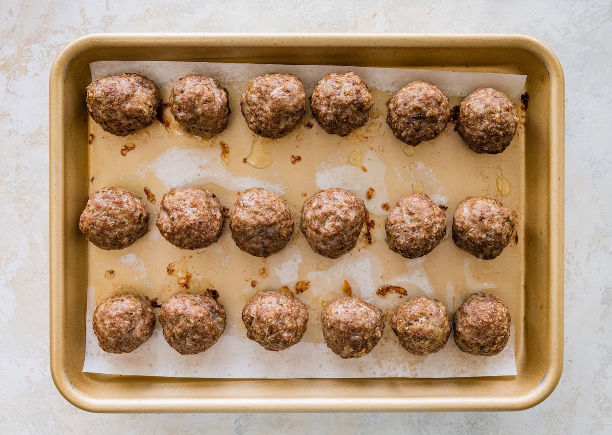 Golden brown baked meatballs fresh from the oven on a sheet pan.