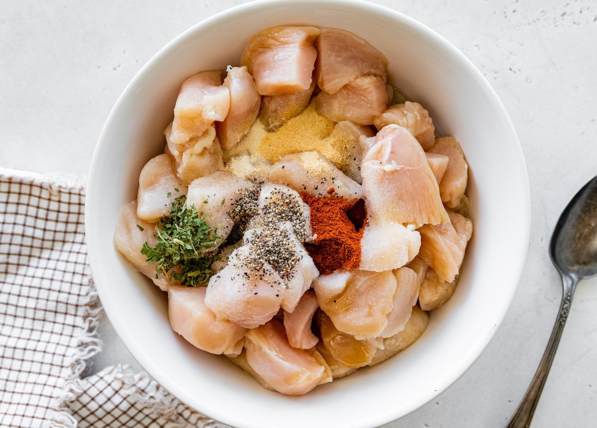 Bowl of raw chicken pieces seasoned with paprika, pepper, garlic powder, and dried herbs.