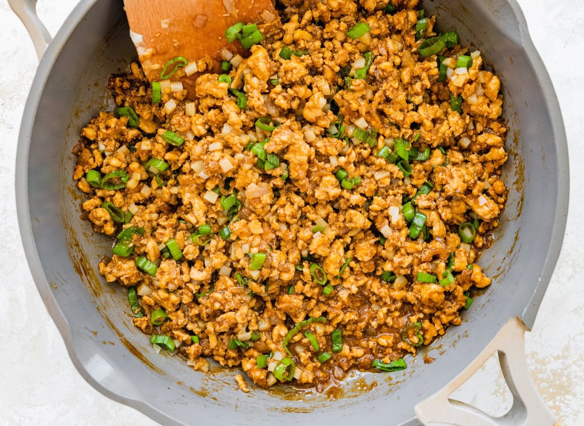 Skillet filled with cooked ground chicken and chopped green onions for lettuce wrap bowls.