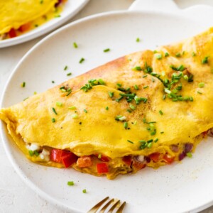 Finished cottage cheese omelette on a plate sprinkled with chives and served with a fork.