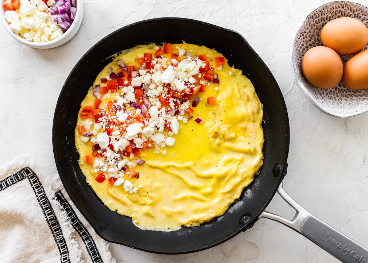 Omelette in a pan Omelette in a pan topped with chopped peppers, red onion and crumbled feta before folding.