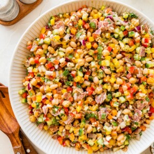 Colorful dense bean salad with beans, salami, feta, and veggies in a white serving bowl.