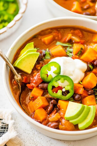 A bowl of sweet potato black bean chili topped with sour cream, jalapeño slices, and avocado.