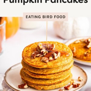 Stack of pumpkin protein pancakes topped with pecans and drizzled with maple syrup on a plate.
