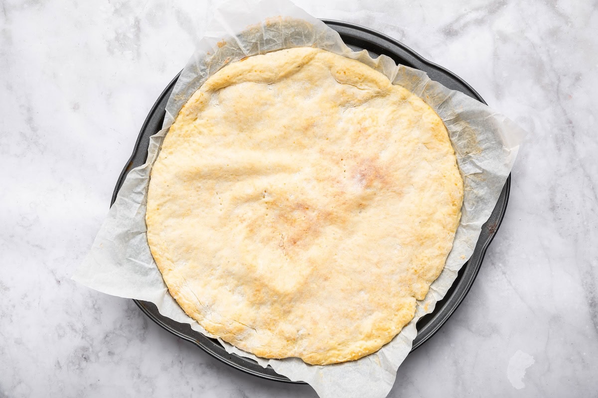 Baked cottage cheese pizza crust in a pizza pan on parchment paper.