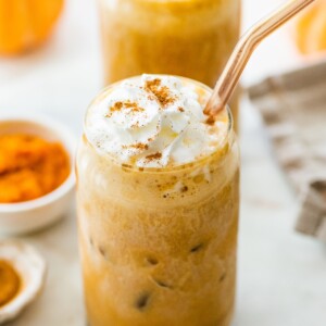 Two iced pumpkin spice lattes with whipped cream and straw.