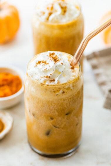 Two iced pumpkin spice lattes with whipped cream and straw.