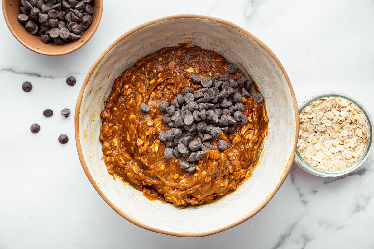 Mixing bowl with pumpkin oatmeal cookie dough and chocolate chips on top.