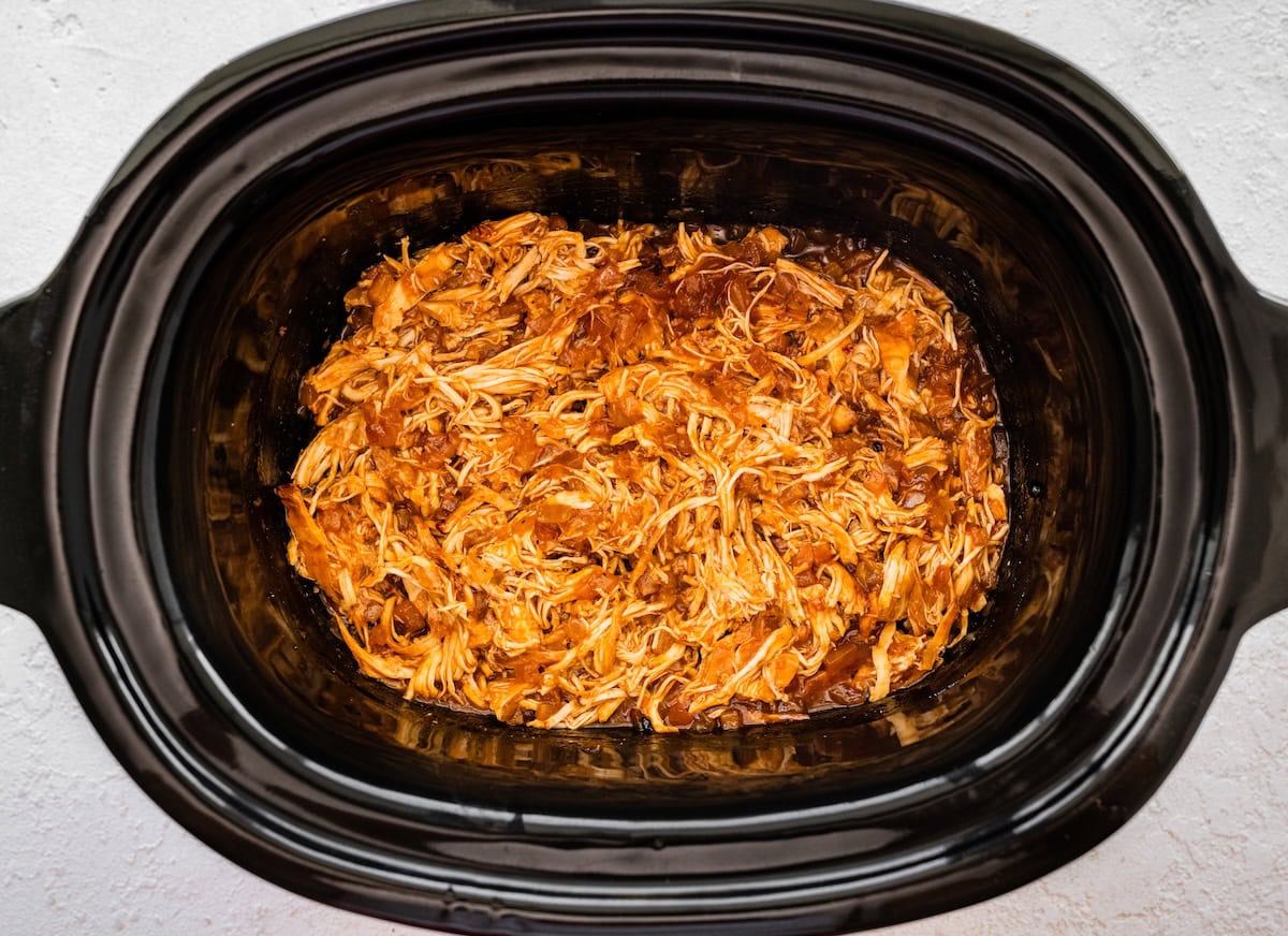 Shredded apple BBQ chicken inside a slow cooker.