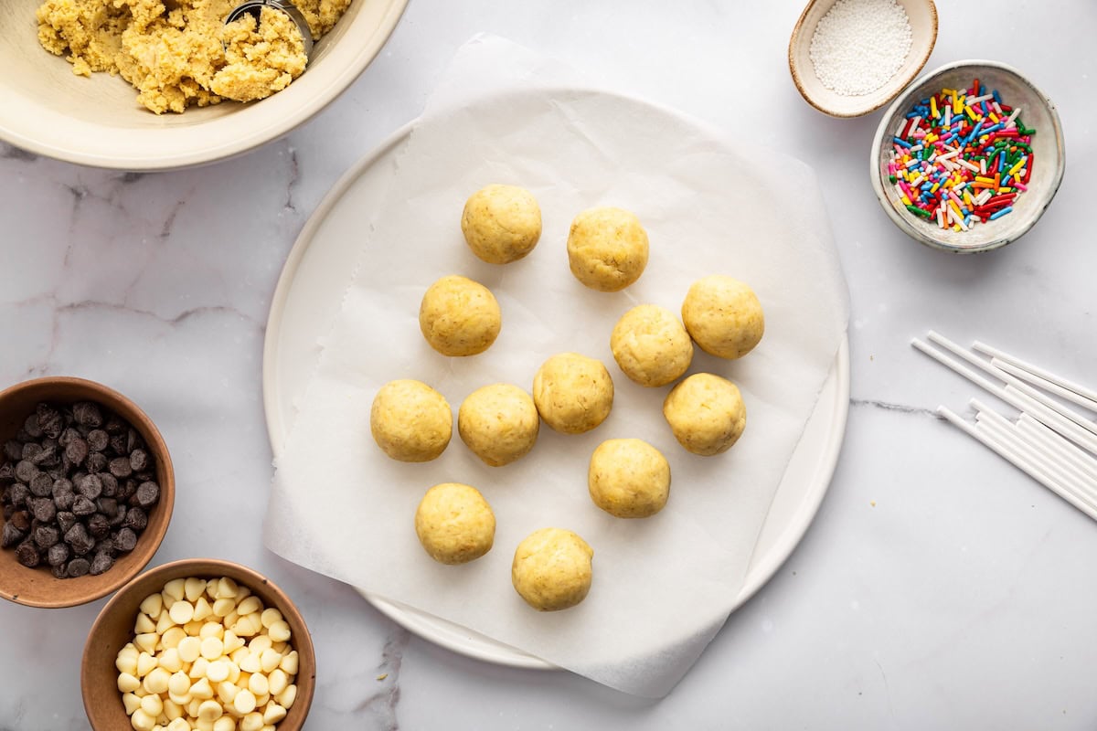 Rolled cake pop balls on a parchment-lined plate ready to be chilled.