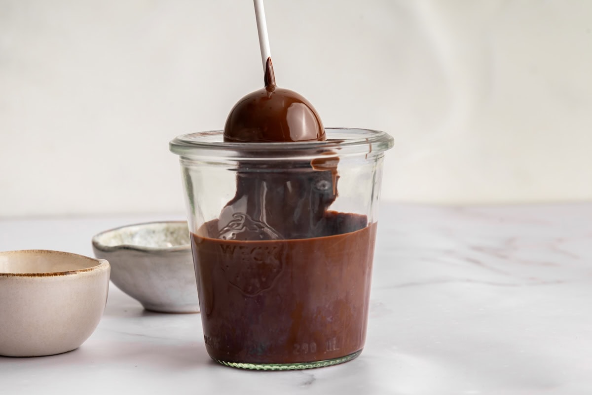 Glass weck jar of melted chocolate with a cake pop stick dipped into the coating.