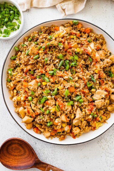 Bowl of homemade chicken fried rice topped with chopped green onions and served on a white table.