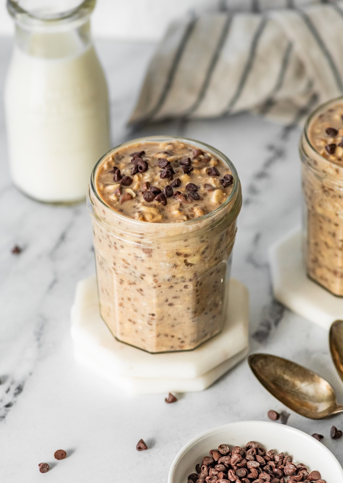 creamy cookie dough overnight oat Single jar of cookie dough overnight oats topped with chocolate chips on a white coaster.